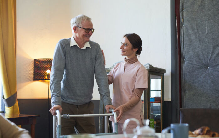 younger nurse helping older gentleman with a walker