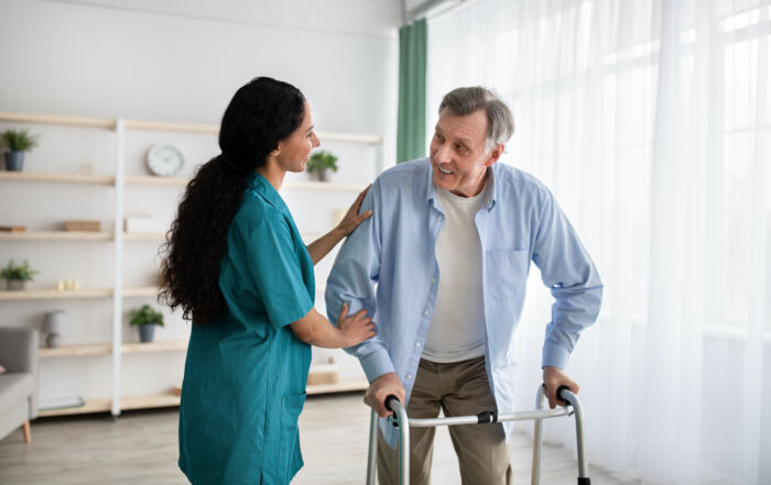 Young nurse helping older man to walk with frame at retirement home
